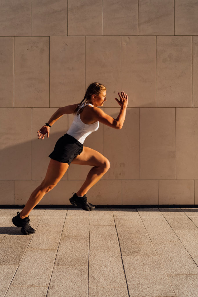 A young adult Caucasian woman is running outdoor crossing modern buildings exterior at sunset.