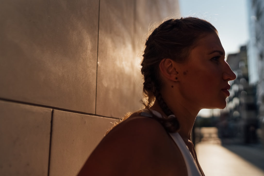 Backlight Portrait of a Beautiful Woman with Braids at sunset. The Sunlight is bouncing on the building a creating a silhouette of her profile. The Female athlete is ready for some running on the city streets.