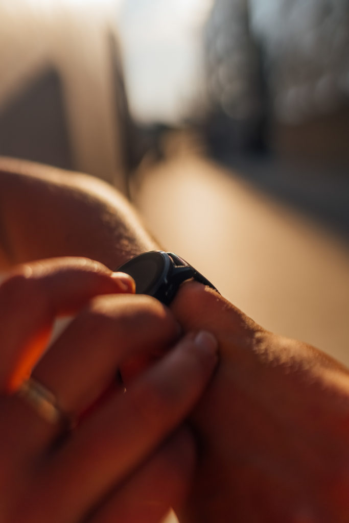 Anonymous Female Hands are interacting with a black sport watch. Fingers are tapping to check the sports activity. Outdoor picture at the sunset