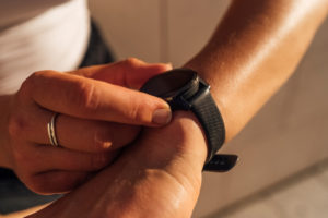 Anonymous Female Hands are interacting with a black sport watch. Fingers are tapping to check the sports activity. Outdoor picture at the sunset
