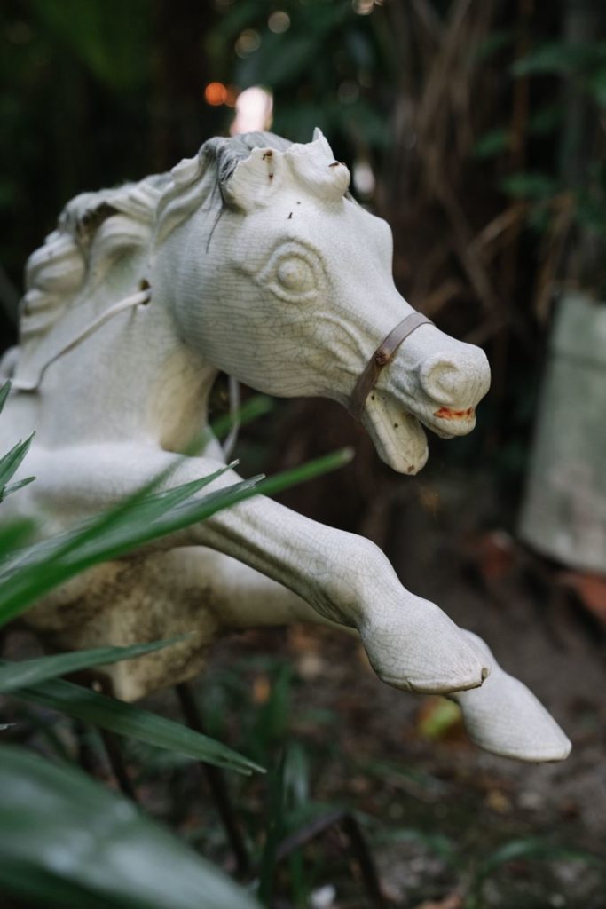 White, old plastic horse toy in the middle of the backyard vegetation. Close up of the fake galloping animal