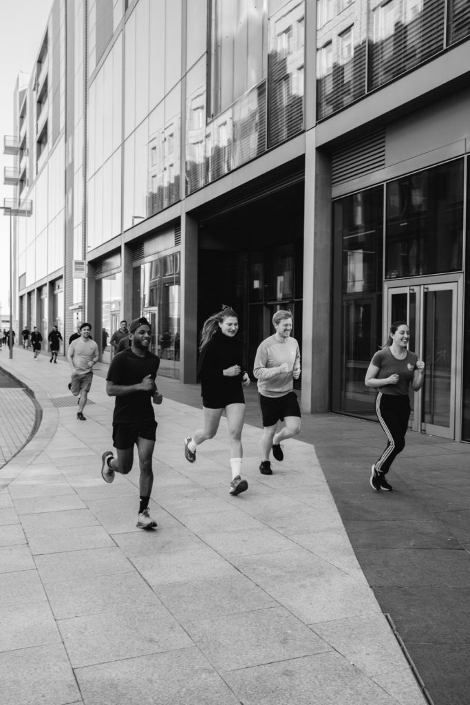 A group of adult people are running in the city, warming up for the Crossfit competition