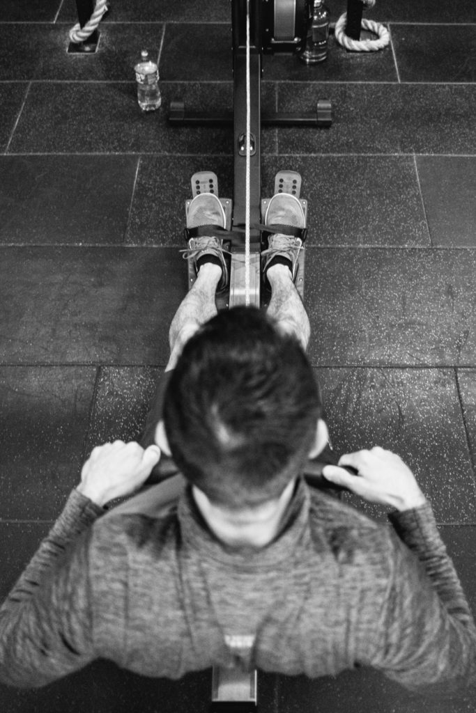Above view of an anonymous man exercising with a Rowing Machine. Black and white picture gym indoor