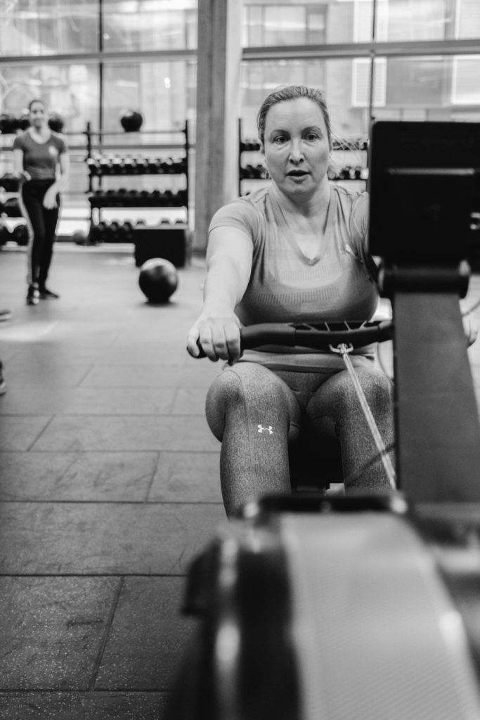 a Real Adult woman is doing exercises Using a Rowing Machine during a Crossfit Competition in the Gym. Black and White image