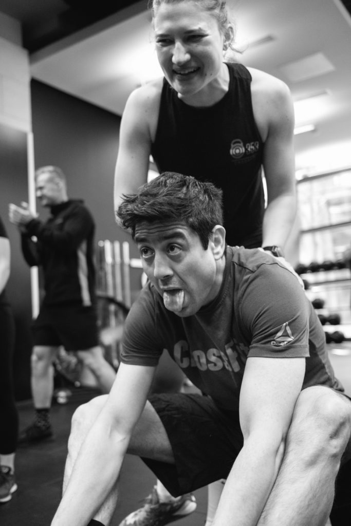 A caucasian woman is cheering her Gym Partner during a cross fit competition at the end of his Rowing Exercise. The man shows his effort by sticking the tough out and looking tired. Black and white image