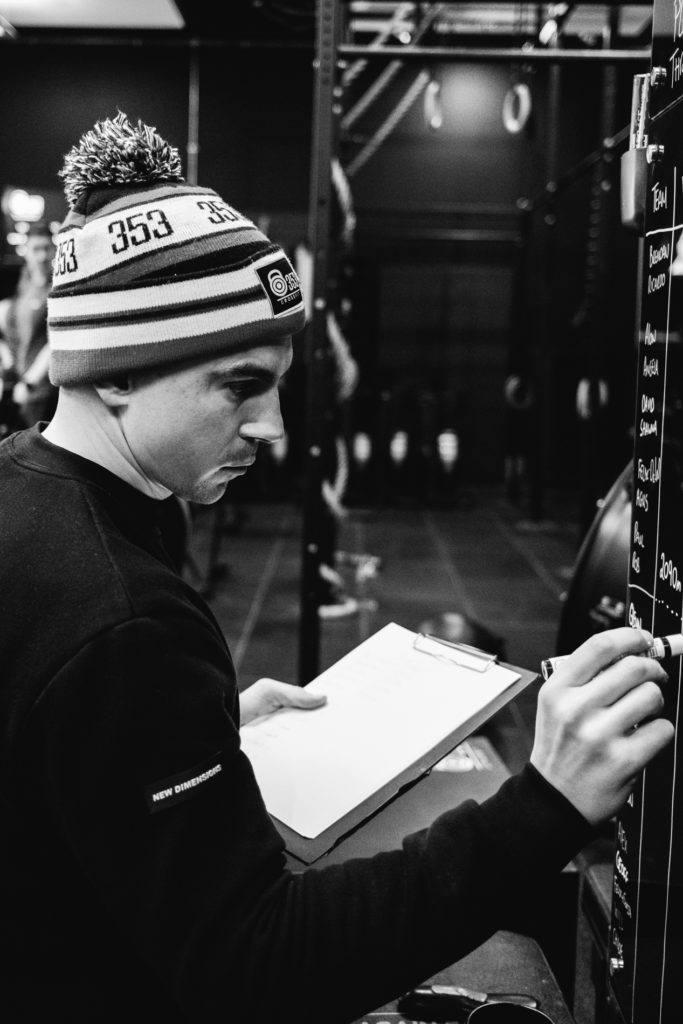 A Caucasian Male Trainer Coach is Wringing on the Crossfit Gym Board results and Exercises from the competition. Black and white image