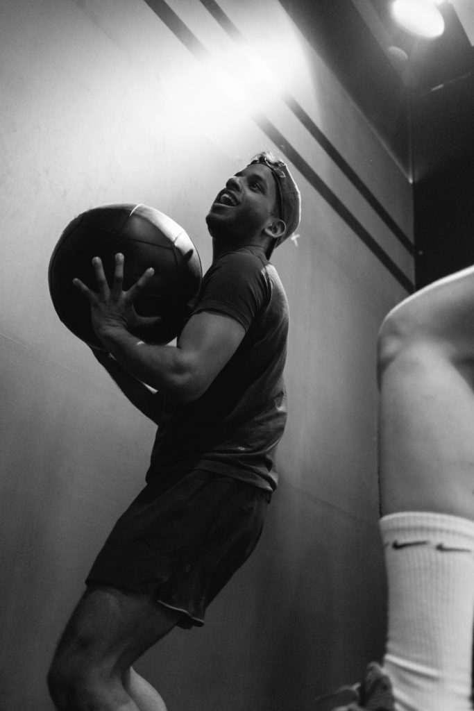 A Black Smiling Man is Training in a Crossfit Gym, Throwing the ball against the wall. Balck and White image