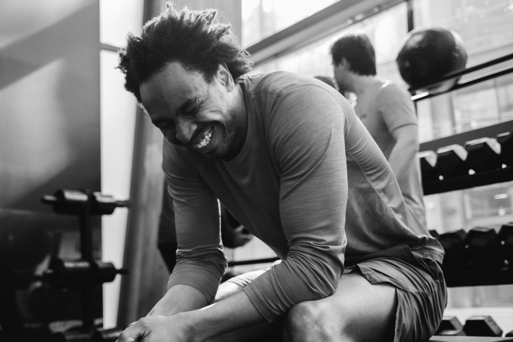 A Smiling Afro Man is sitting at the Gym during the Break. Black and White image