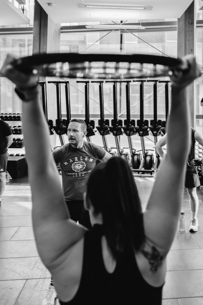 A man is looking at the other team during his Female Teammate is lifting and finishing her exercise. The Athlete is framed between the lited arms. Back and white image