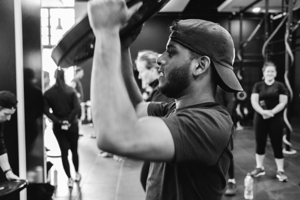 A young black man, Portrait, who is wearing a baseball cap, is lifting a Disk Weight during a Crossfit competition.
