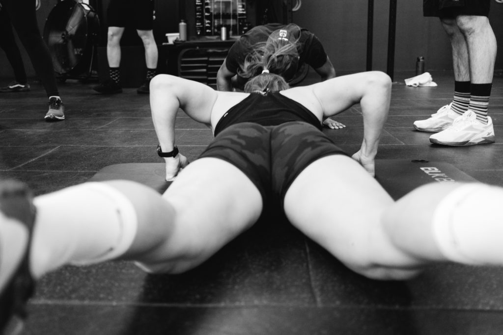 Man and Woman in the same team are doing Push ups during a Crossfit competition. Ground Level view from the back of the woman. Back and White image