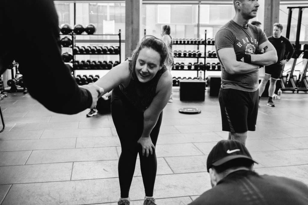 A tired Real Woman is Cheering and Smiling while doing a Fistbump with an Anonymous Crossfit Team mate. Black and White indoor image