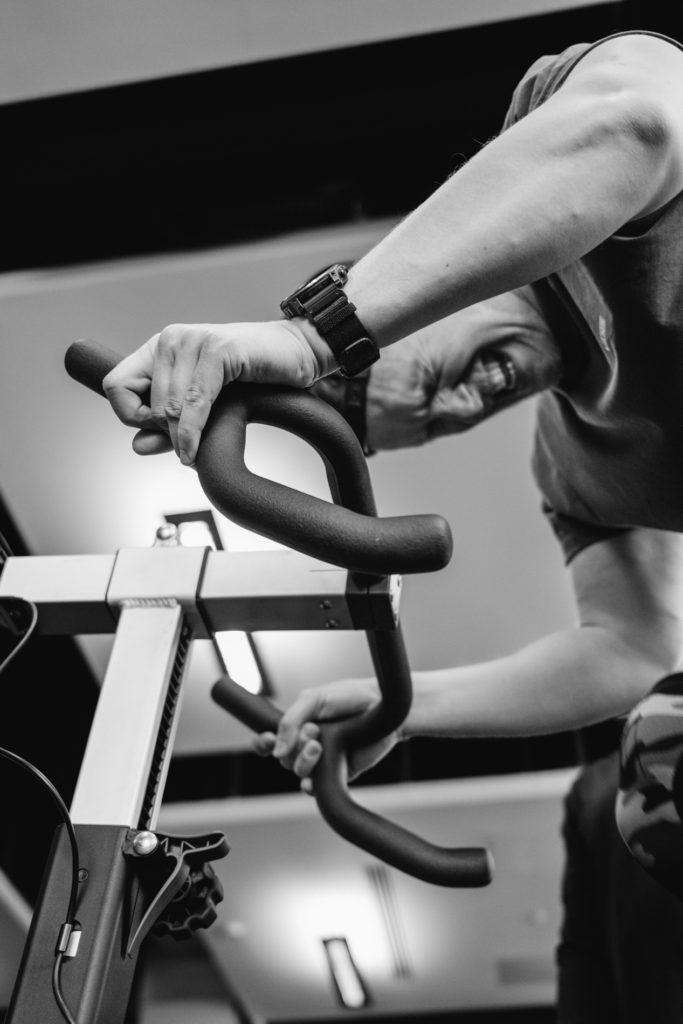 A man with a struggling Face is Pushing Hard on the Bike during a Crossfit Competition. Low angle view focuses on the Hands. Black and White image