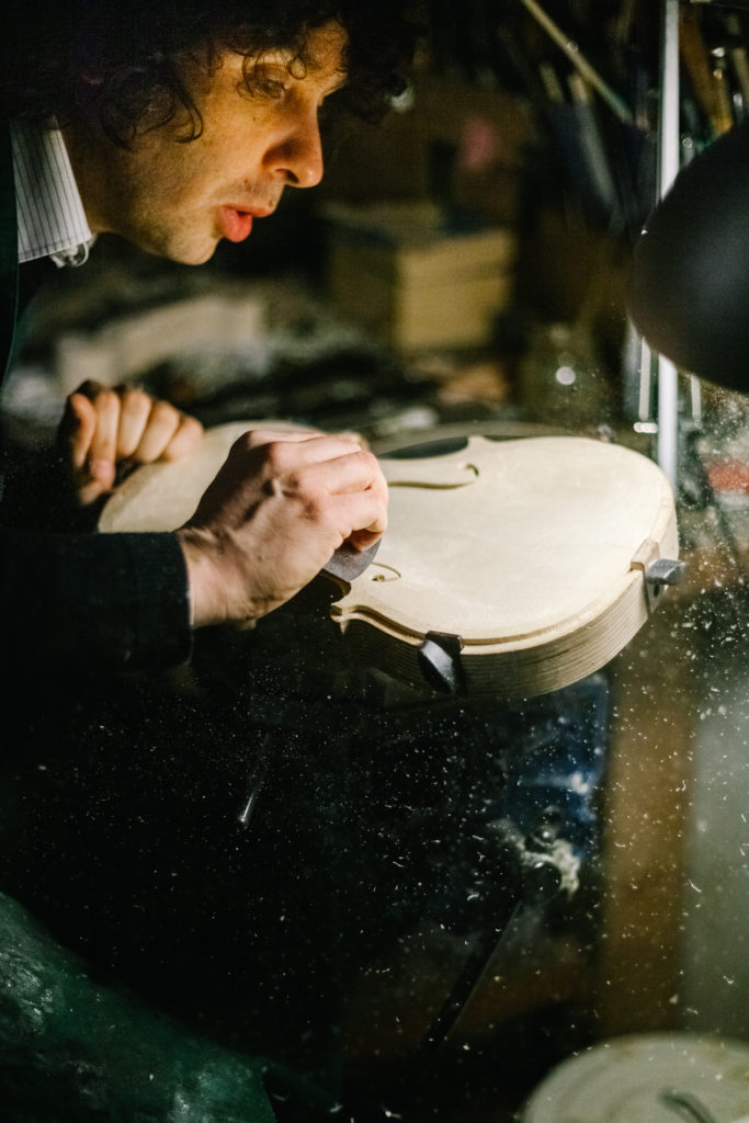 An Italian Violinmaker Portrait while he blows the Wooden Chips and Dust from a Handmade Violin