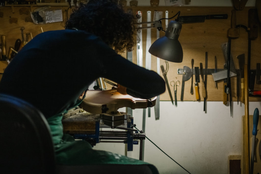An Anonymou Italian Violinmaker sits on his work desk and working carefully part of a Handmade Violin carefully part of a Handmade Violin
