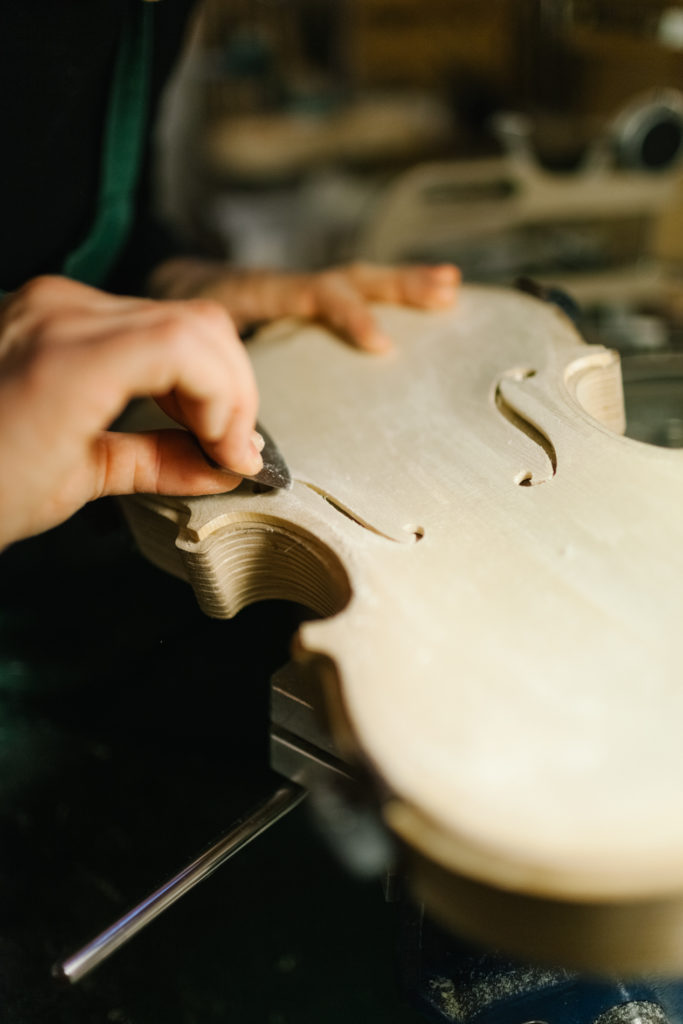 An Anonymous Italian Violinmaker sits on his work desk and sanding carefully part of a Handmade Violin