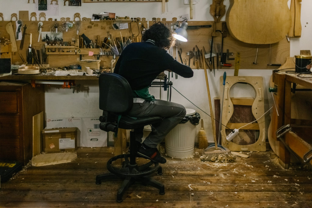 An Anonymous Italian Violinmaker sits at his work desk and works carefully on the part of a Handmade Violin.