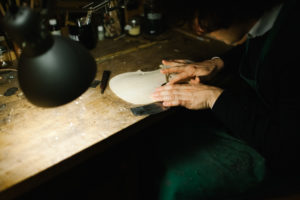 An Anonymous Italian Violinmaker sits on his work desk and sanding carefully part of a Handmade Violin.