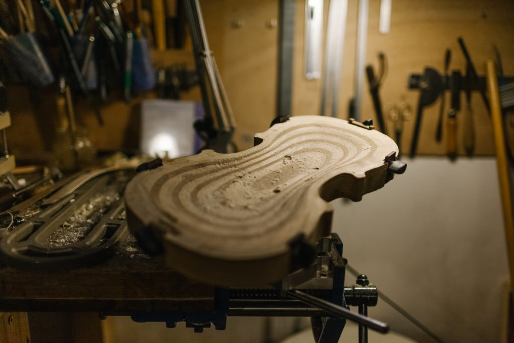 A work in progress violin on a vise. The wooden musical instrument is sull of dust and chimps from the handmaking preparation.