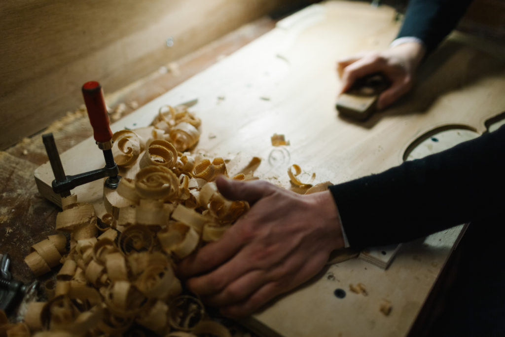 Close up of Hands Scraping a Wooden Board to create a Violin