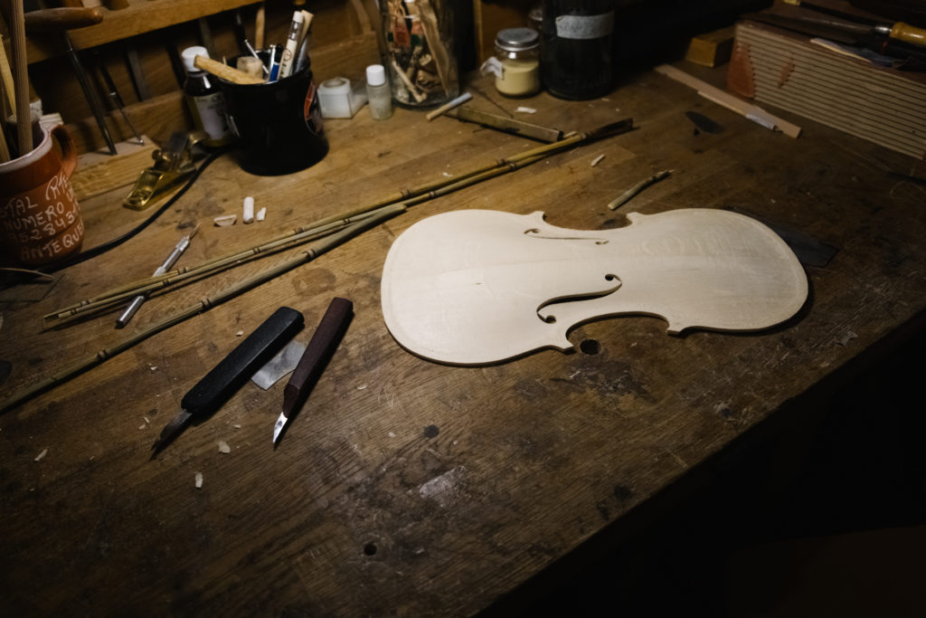A wooden board is Outlined as a Violin. Violinmaker Workshop detail with Lamp Spotlight