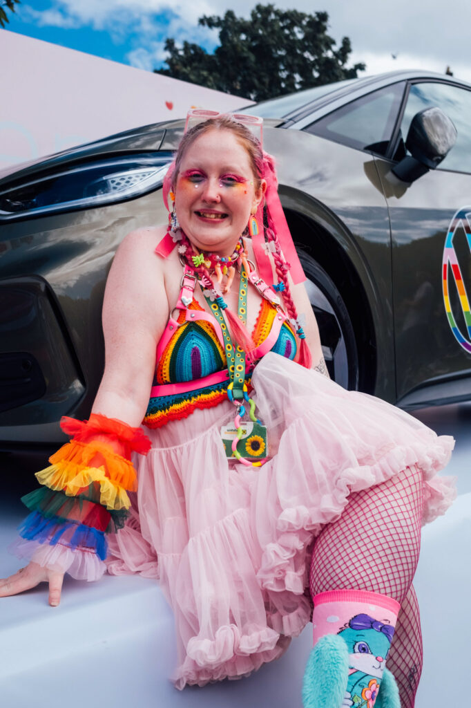 A colourful parade-goer in vibrant rainbow attire poses in front of a VW ID.4 at the Dublin Pride Parade.