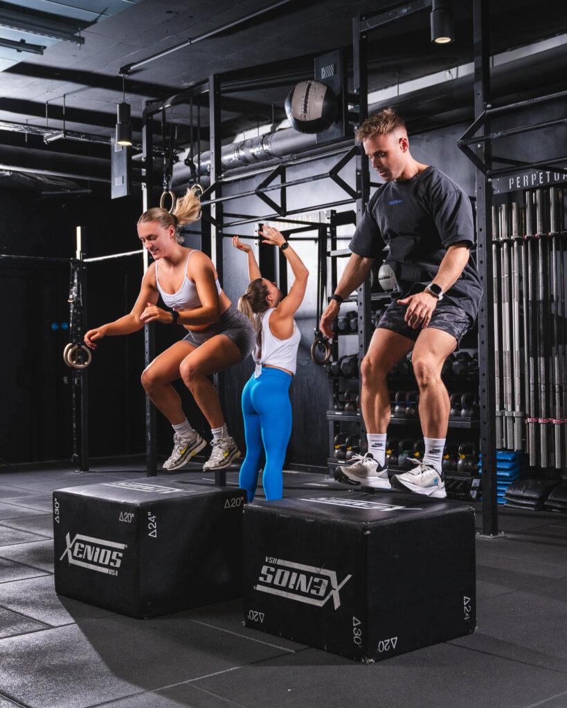 hree people performing box jumps during a fitness class at Perpetua Gym Dublin.