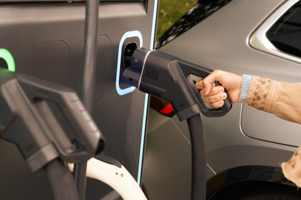 Close-up of a person plugging an electric vehicle charger into a grey car.