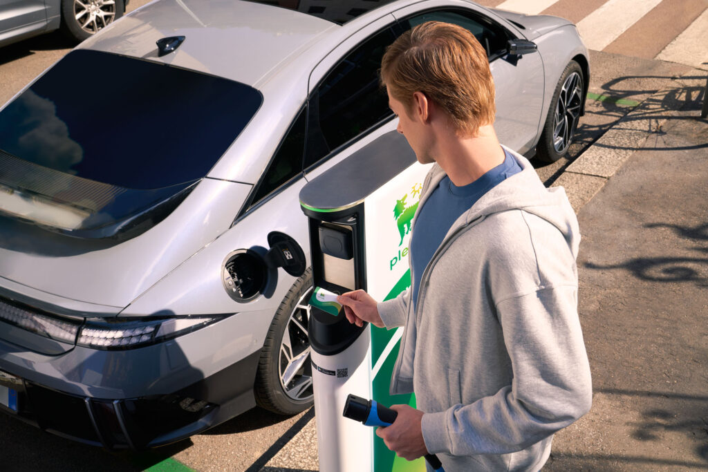 Young man plugging electric car at Plenitude-Eni charger smiling