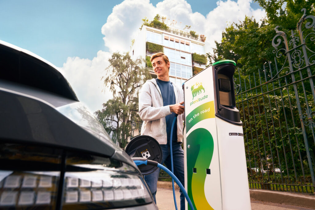 Man charging an electric car at Plenitude-Eni charging station, holding RFID card and cable