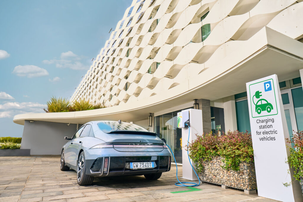 Electric Hyundai Ioniq 6 charging at Plenitude station outside modern hotel