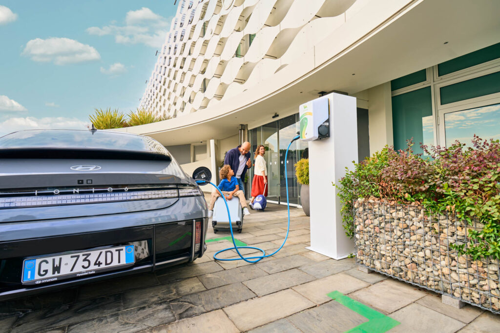 Family arriving at a hotel with their electric car charging at a Plenitude station