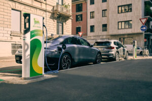 Two electric cars charging at Plenitude stations on a quiet European city street.